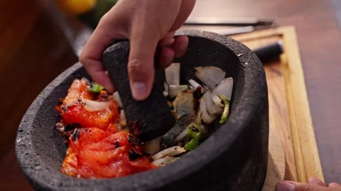 Chef grinds and prepares fresh roasted mexican salsa in a stone molcajete bowl Stock Footage 288038820