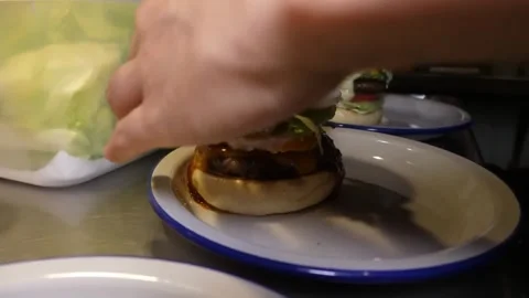 Chef Hand Assembling a Gourmet Burger on a White Plate, Close-Up Stock-Footage 347687748