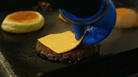 Chef Hand Placing Cheese Slice on Sizzling Beef Burger Patty on Hot Grill Stockbeeldmateriaal 332684038