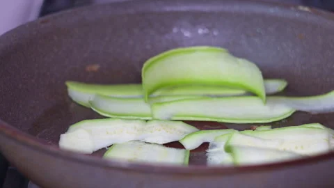 Chef Hand Placing Thin Sliced Zucchini Strips into Hot Frying Pan on Kitchen Stock Footage 339629629