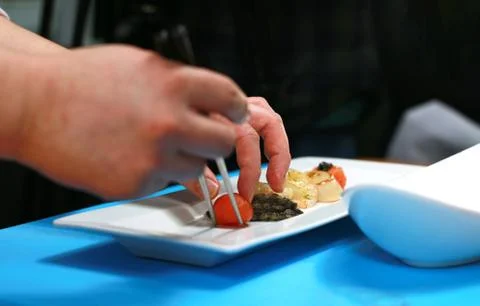 Chef hand putting a fresh cherry tomato on a sea food dish. Stock Photos