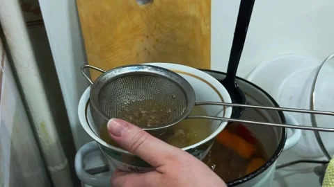 Chef hand straining ladled broth through sieve, close-up Stock Footage 336533894