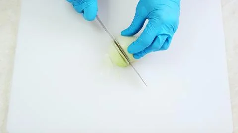 Chef hands in blue gloves slice half onion closeup Stock Photos