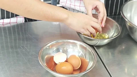 Chef hands cracking a fresh brown egg into a mixing bowl. Stockbeeldmateriaal 339200632
