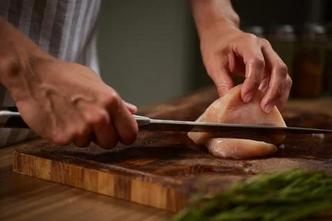 Chef hands cutting raw chicken breast on board Stock Photos