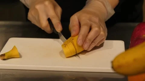 Chef Hands with Gloves Slicing Fresh Yellow Banana on White Cutting Board Stock Footage 345292909