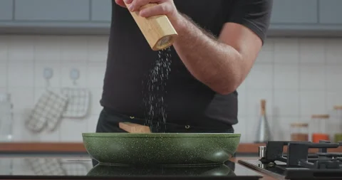 Chef hands grinding salt on the dish. Male chef salting dish in a frying pan Stock Footage 263671256