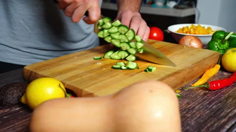 Chef hands in home kitchen cutting a cucumber on a wooden cutting board. Stock Footage 302299912