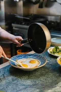 Chef hands plating fried eggs on a ceramic dish Stock Photos