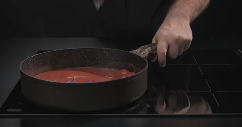 Chef hands put basil into Italian tomato sauce on a black background Stock Footage 249990936