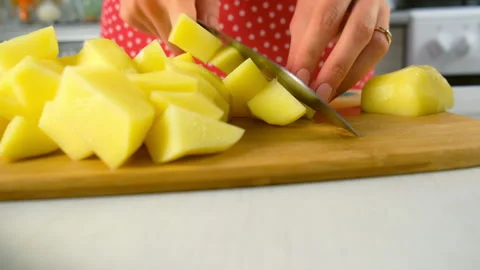 Chef hands skillfully slicing fresh potatoes into cubes on wooden cutting board. Stock Footage 312402224