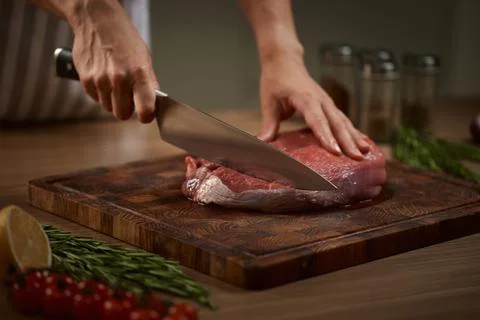 Chef hands slicing raw beef on cutting board Stock Photos