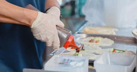 Chef hands squeezing sauce onto wraps, commercial kitchen food prep Stock Footage 343057704