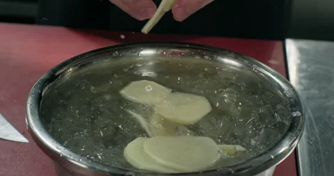 Chef hands washing sliced potato in a cold water with ice, preparing a meal Stock Footage 294229379