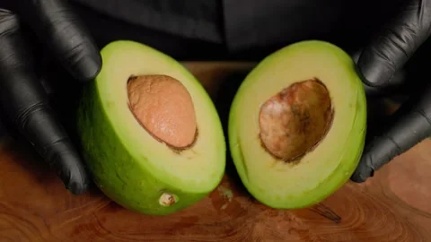 Chef holding halved avocado with seed on wooden board in black gloves Stock Footage 312814882
