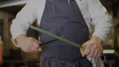 A chef is holding a knife and a sword, preparing to cut something Stock Footage 306577089