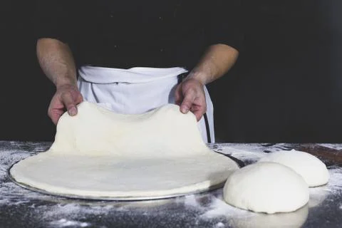 Chef holding uncooked pizza with on table in black background. Stock Photos
