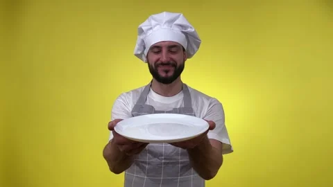 Chef holding white empty plate delighted good smell isolated on yellow Stock Footage 234813107