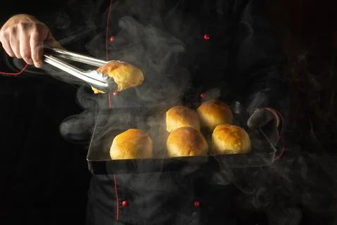 A chef holds a baking sheet of freshly baked buns. Steam rises from the bak.. Stock Photos