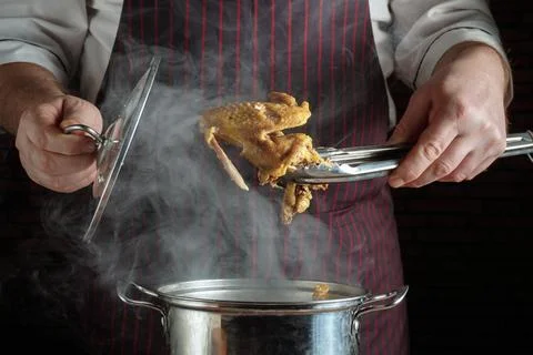 A chef holds a pair of tongs while lifting a cooked chicken from a pot. Steam Stock Photos