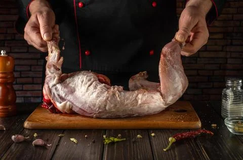 A chef holds a raw rabbit with both hands above a wooden cutting board. Ing.. Stock Photos