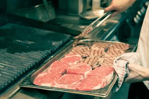 Chef in hotel or restaurant kitchen grilling pork for luxury dinner party wit Stock Photos