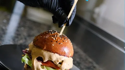Chef inserting a wooden stick into a hamburger in the kitchen black background Stock Footage 230076147