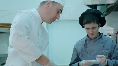 Chef instructing trainee in the kitchen while he is taking notes Stock Footage 72326779