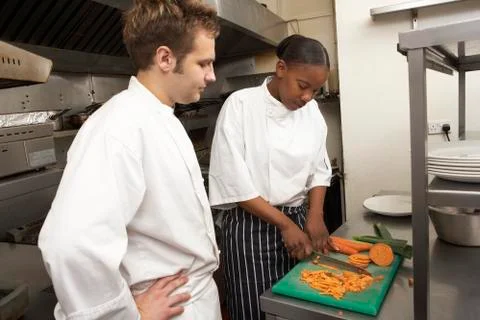 Chef Instructing Trainee In Restaurant Kitchen Stock Photos