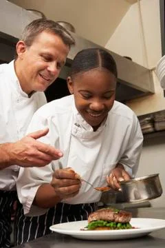 Chef Instructing Trainee In Restaurant Kitchen Stock Photos