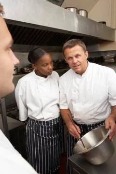 Chef Instructing Trainees In Restaurant Kitchen Stock Photos