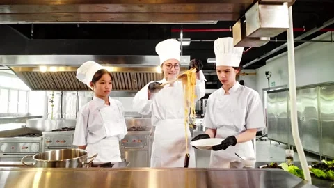 Chef instructor guides two young culinary students in plating pasta during cook Stock Footage 314324584