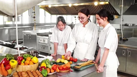 Chef instructor teaching two young culinary students in a commercial kitchen Stock Footage 313587310