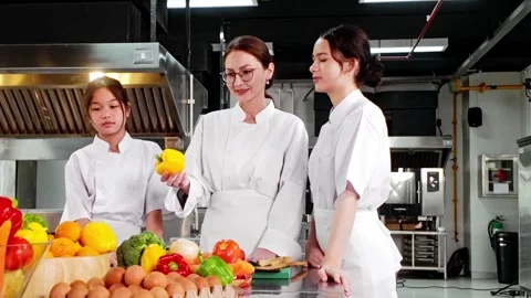 Chef instructor teaching two young culinary students in a commercial kitchen 動画素材 328076856