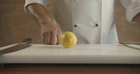 Chef in the kitchen cuts yellow lemon with sharp knife in half Stock Footage 103841421