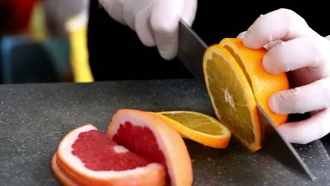 Chef in kitchen slicing fresh orange on cutting board Stock Footage 98763806