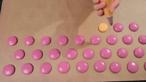 Chef make of a pink and orange macaroons, pour the filling on the baking paper. Stock Footage 148536698
