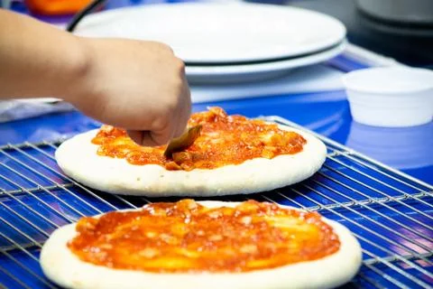 Chef making pizza at kitchen, Chef spreading cheese toppings on pizza base Stock Photos