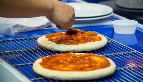 Chef making pizza at kitchen, Chef spreading cheese toppings on pizza base Stock Photos