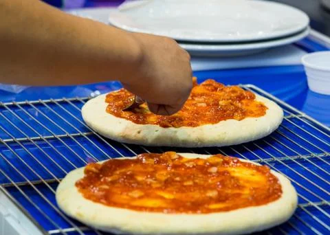 Chef making pizza at kitchen, Chef spreading cheese toppings on pizza base Stock Photos