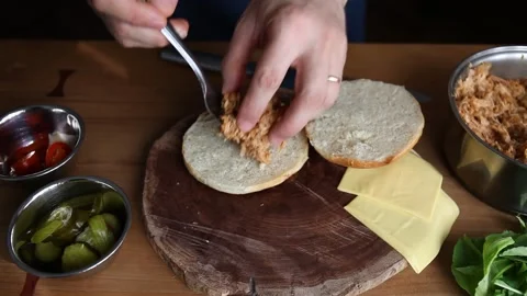 Chef making a pulled pork sandwich on a fresh roll loads meat, cheese, pickles Stock Footage 147219038