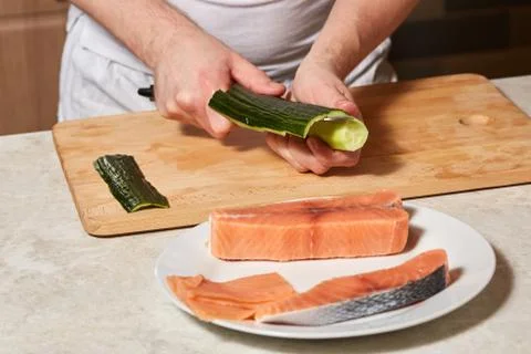 Chef making sushi rolls. Cutting cucumber and salmon fish Stock Photos
