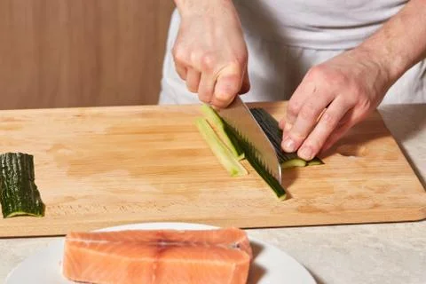 Chef making sushi rolls. Cutting cucumber and salmon fish Stock Photos