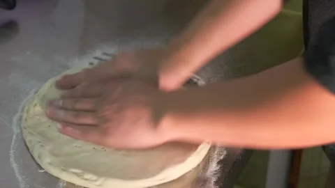 A chef manually rolls pizza dough into a flat circle in a pizzeria kitchen. Stock Footage 279942805