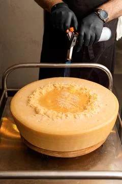 Chef melts cheese using a hand-held gas burner, head of Parmesan cheese, se.. Stock Photos
