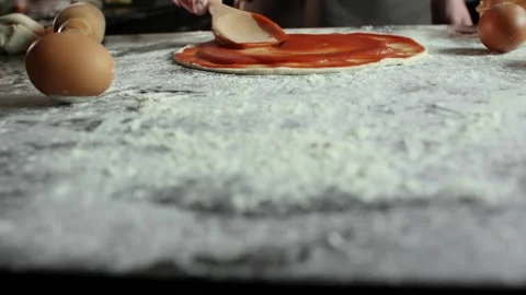 Chef men spreads tomato paste on pizza dough in the kitchen table Video stock 105418117