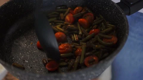 Chef mixes fried green beans and cherry tomatoes with a black plastic spoon Stock Footage 159268483