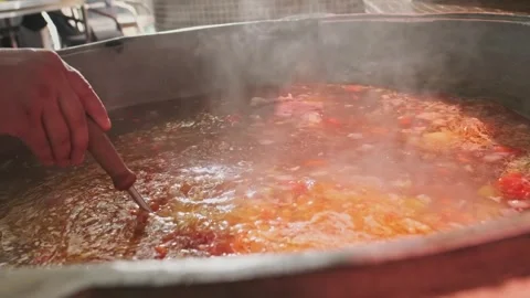 Chef mixes meat soup with vegetables in a large cauldron with a slotted spoon Stock Footage 263102022