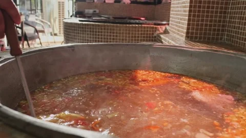 Chef mixes meat soup with vegetables in a large cauldron with a slotted spoon Stock Footage 280462505