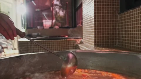 Chef mixes meat soup with vegetables in a large cauldron with a slotted spoon Stock Footage 307767703